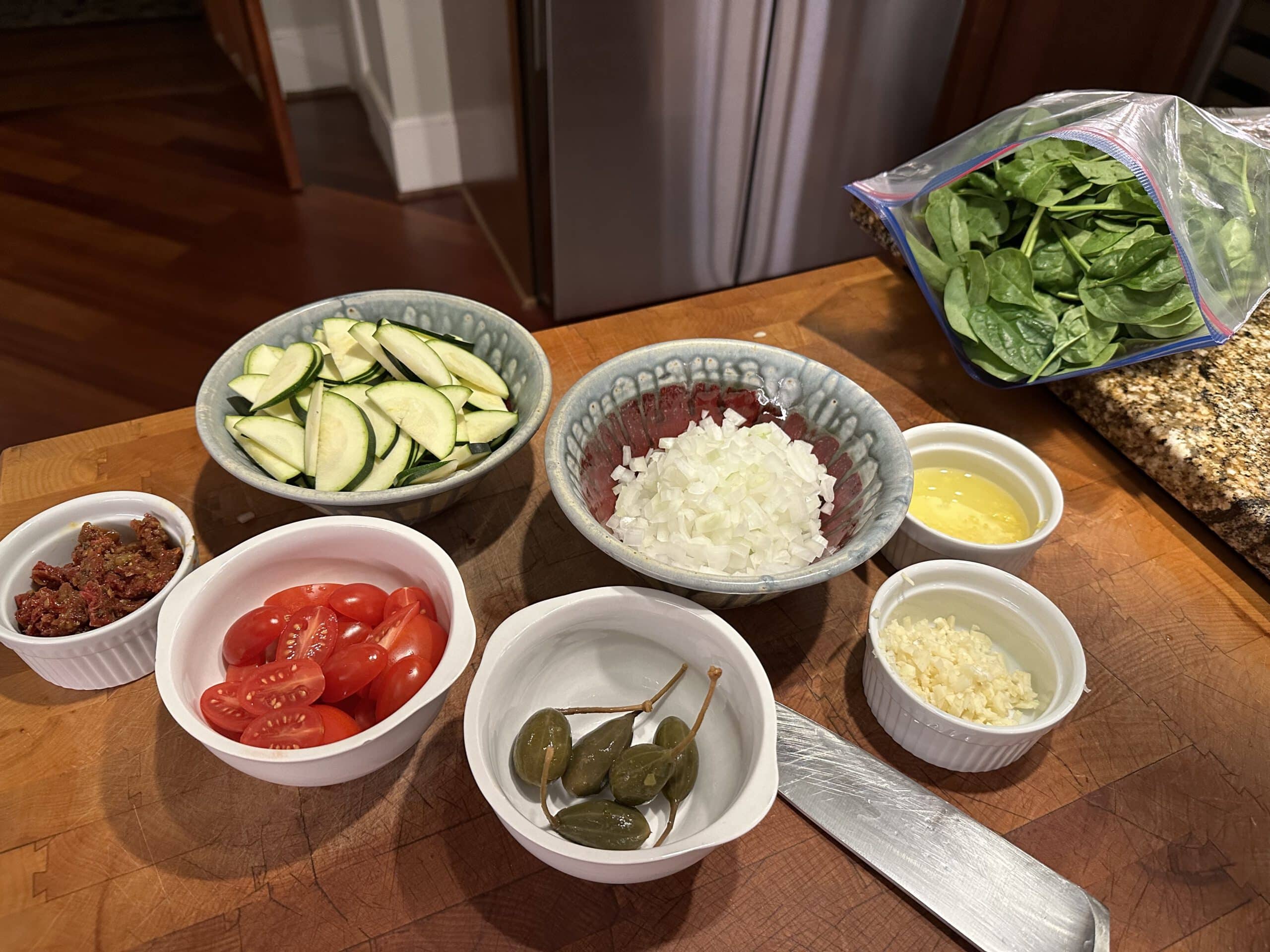 Ingredients for pasta primavera prepped and ready for use in bowls on a wood butcher block