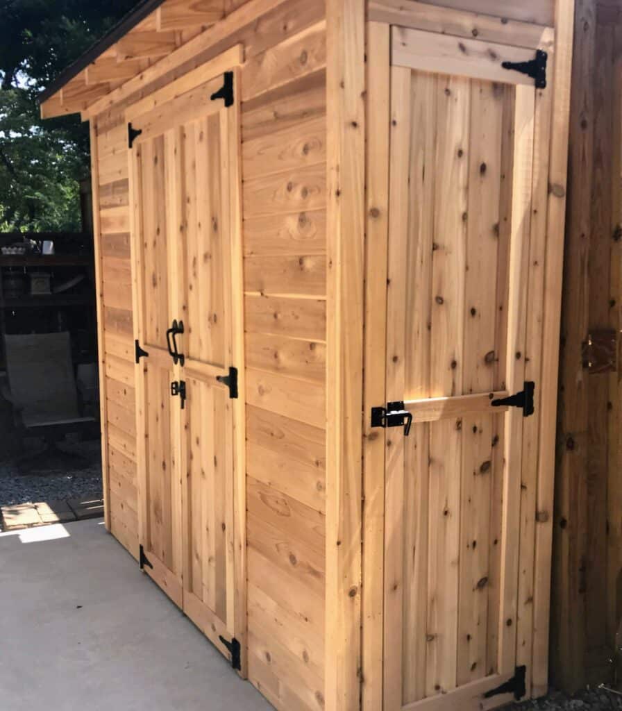 wood-sided shed showing closet door on one end designed to hold tools and supplies