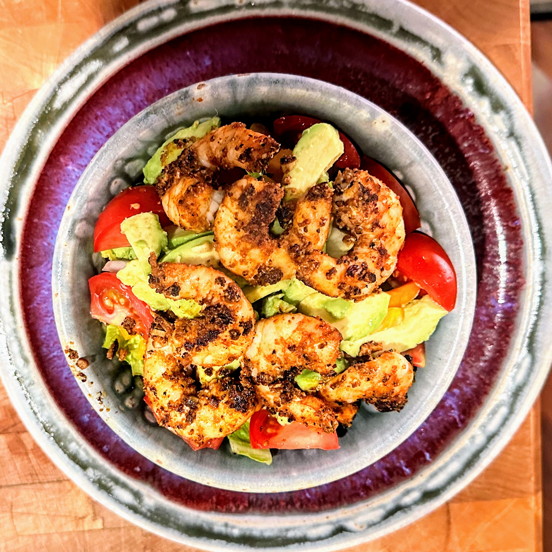 red and gray bowl full of BBQ shrimp with veggies peaking through