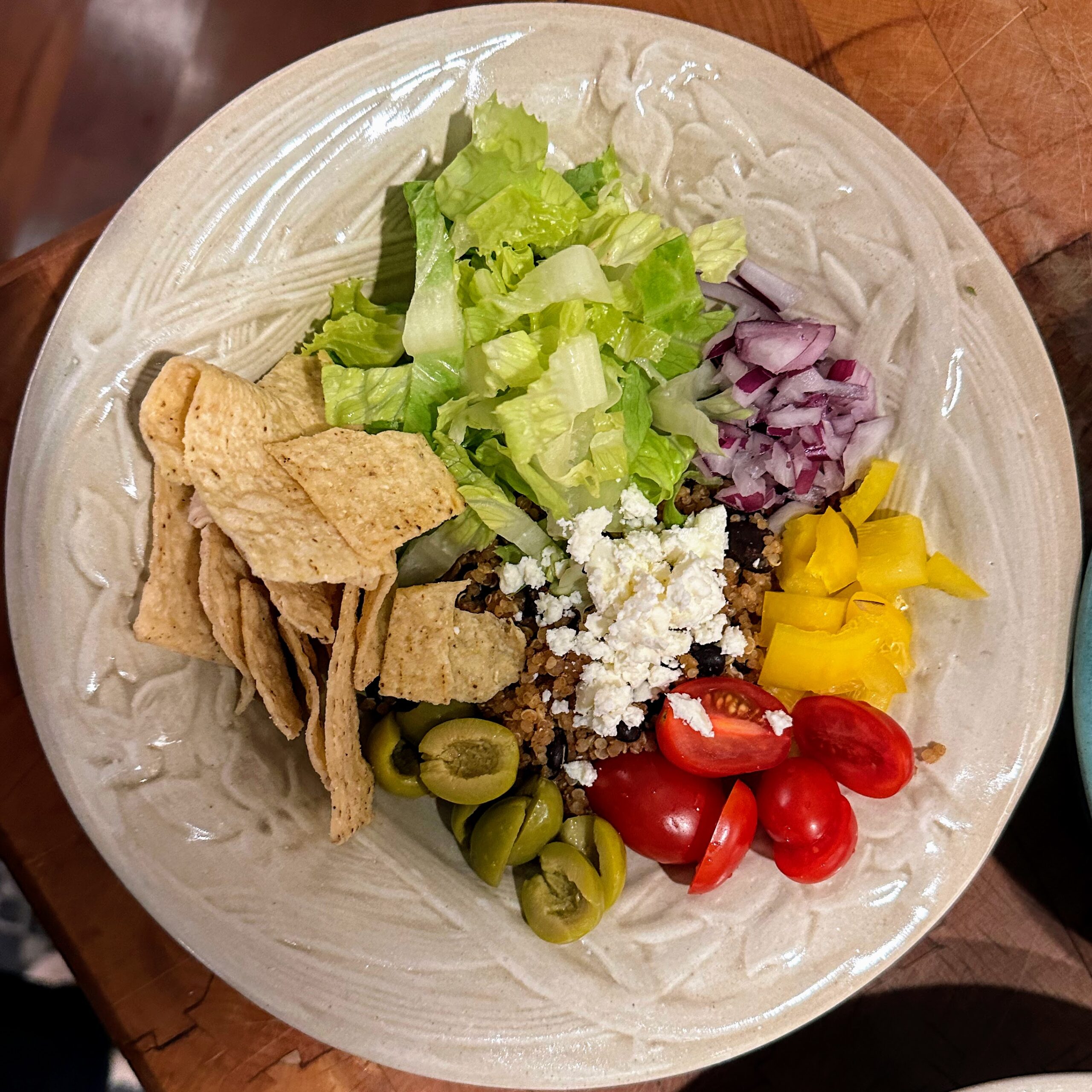 Mexican beans and rice in a white pottery bowl topped with lettuce, onions, tomatoes, olives and cheese