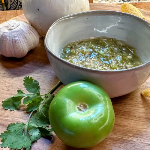 Salsa Verde in a grey pottery bowl on a wood tray surrounded by fresh veggies